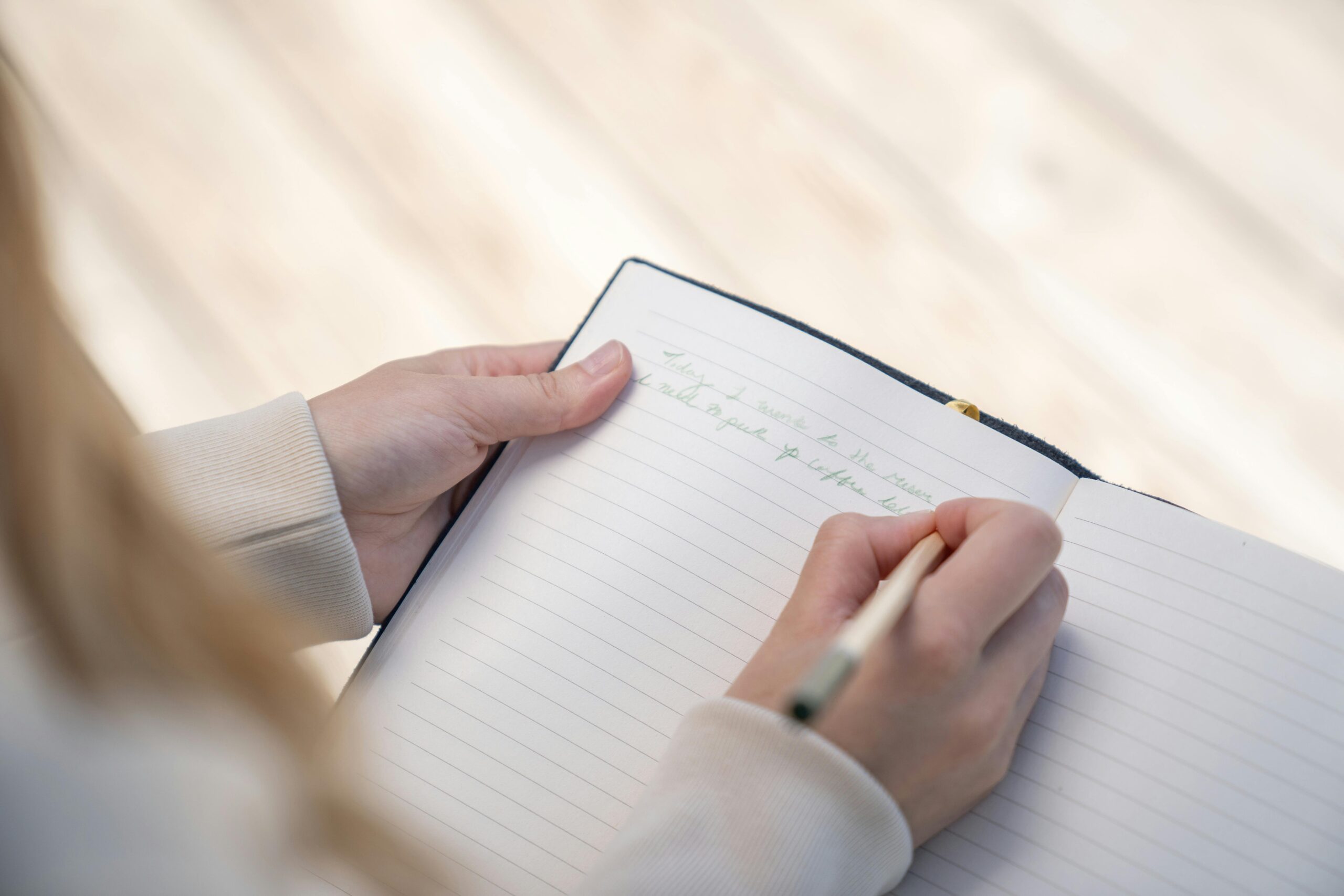 A person writing in a notebook with a pen, capturing a close-up view of hands.